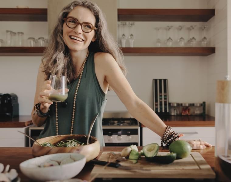 Woman enjoying mpowder shake in a modern kitchen with fresh vegetables and healthy ingredients on the counter small